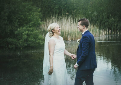 Brudepar griner til hinanden, de står foran en sø og er fotograferet ved Davinde i Odense