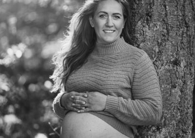 Sort hvid billede af gravid dame der staar op af et trea