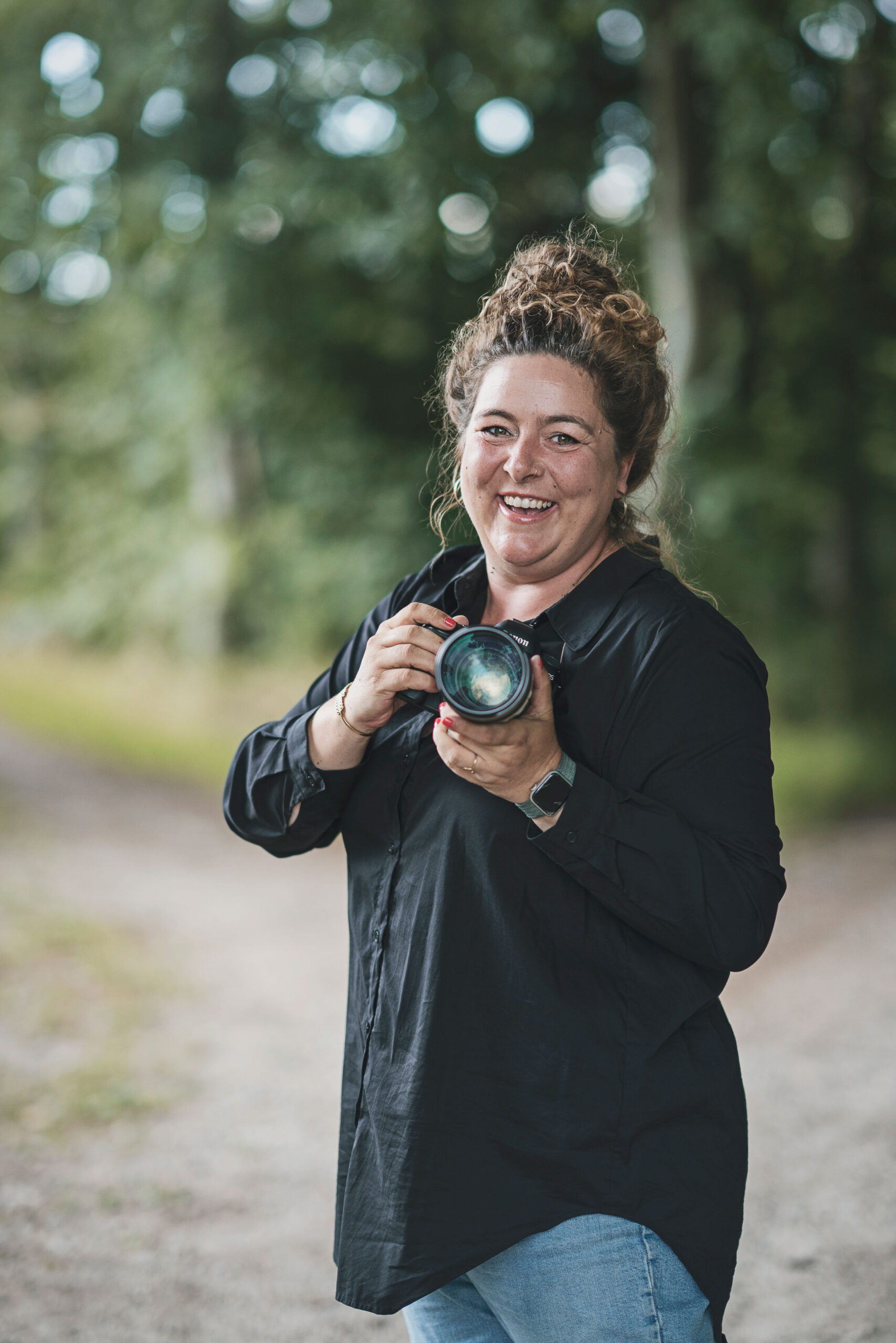 billede af fotograf winnie synia med kameraet i hånden. hun står i en skov på fyn og smiler